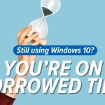 A hand holds an hourglass against a blue background. Text reads: Still using Windows 10? YOU’RE ON BORROWED TIME—Windows 10 extended support ends in October 2026. A stylized A logo appears in the top right corner.